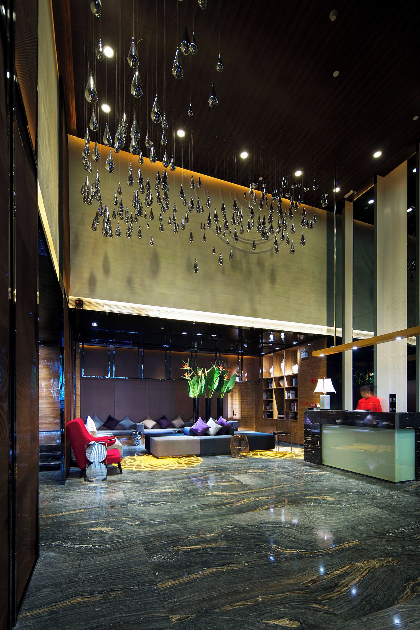 A modern lobby with a seating area, a reception desk, and a decorative ceiling with hanging elements.
