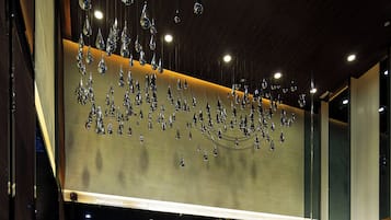 A modern lobby with a seating area, a reception desk, and a decorative ceiling with hanging elements.