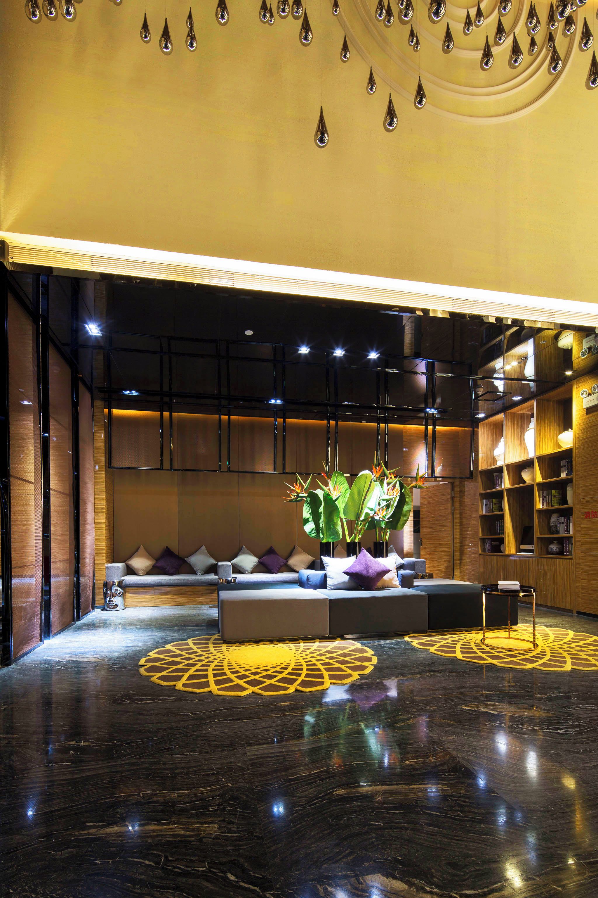 Een moderne lobby met een donkere marmeren vloer, een zithoek met kussens en een grote plant.