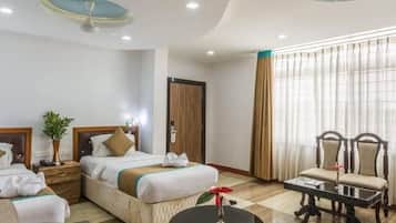 Habitación de hotel con dos camas, una zona de estar con sillas, una mesita y un ventanal grande con cortinas.