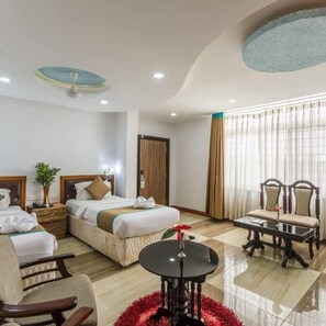 A hotel room with two beds, a sitting area with chairs, a small table, and a large window with curtains. - Hotel Jaya Grand  (Guntur)
