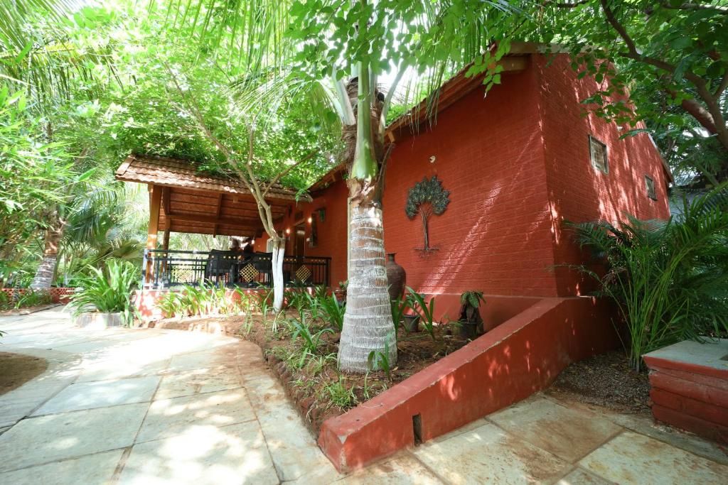 A red brick building with a covered patio area, surrounded by lush greenery and a stone pathway.
