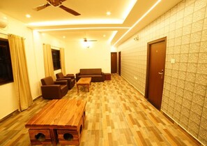 A hotel room with a wooden floor, a ceiling fan, a sofa set, a coffee table, and a patterned wall. - Brown Town Resort Spa and Convention  (Hyderabad)