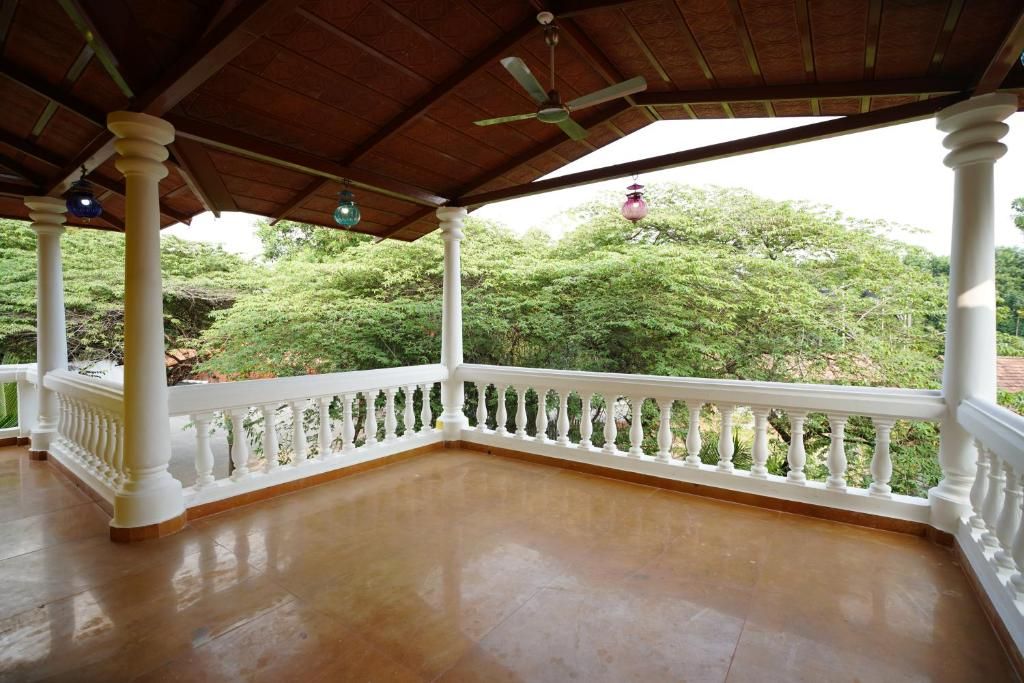 Un espacio al aire libre techado, con techo de madera, balaustradas blancas y vistas a la vegetación.