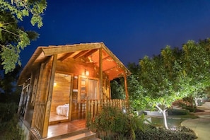 A wooden cabin with a porch, a bed, and a small garden area. - Brown Town Resort Spa and Convention (Hyderabad)