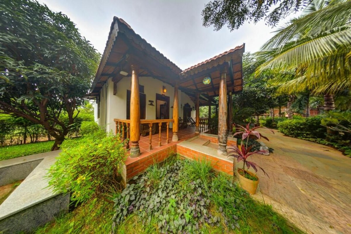 Una casa tradicional con techo de tejas, un porche con barandillas de madera y un jardín con diversas plantas.