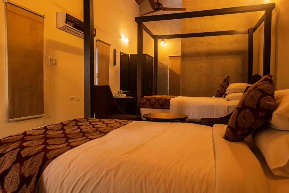 Habitación de hotel con cama con dosel, un escritorio con silla y una pequeña mesa redonda.