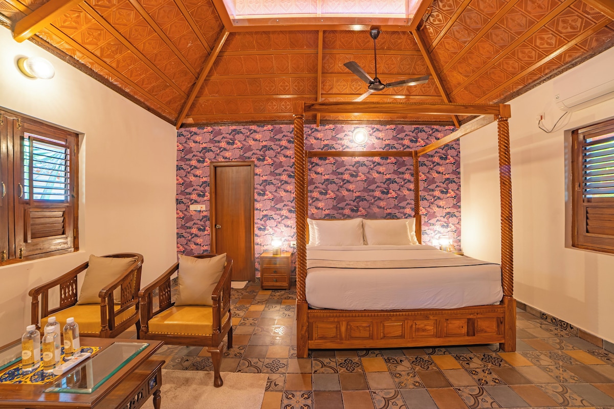 A four-poster bed with a canopy, a wooden ceiling, and patterned wallpaper.