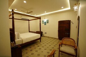 A four-poster bed with a wooden frame, a ceiling fan, recessed lighting, a wooden wardrobe, and a rattan chair.