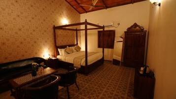 A four-poster bed with a wooden frame, a small table with a vase, a chair, and a cabinet in a room with patterned wallpaper and a tiled floor.