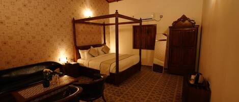 A four-poster bed with a wooden frame, a small table with a vase, a chair, and a cabinet in a room with patterned wallpaper and a tiled floor.