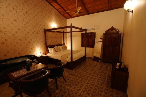 A four-poster bed with a wooden frame, a small table with a vase, a chair, and a cabinet in a room with patterned wallpaper and a tiled floor. - Brown Town Resort Spa and Convention (Hyderabad)