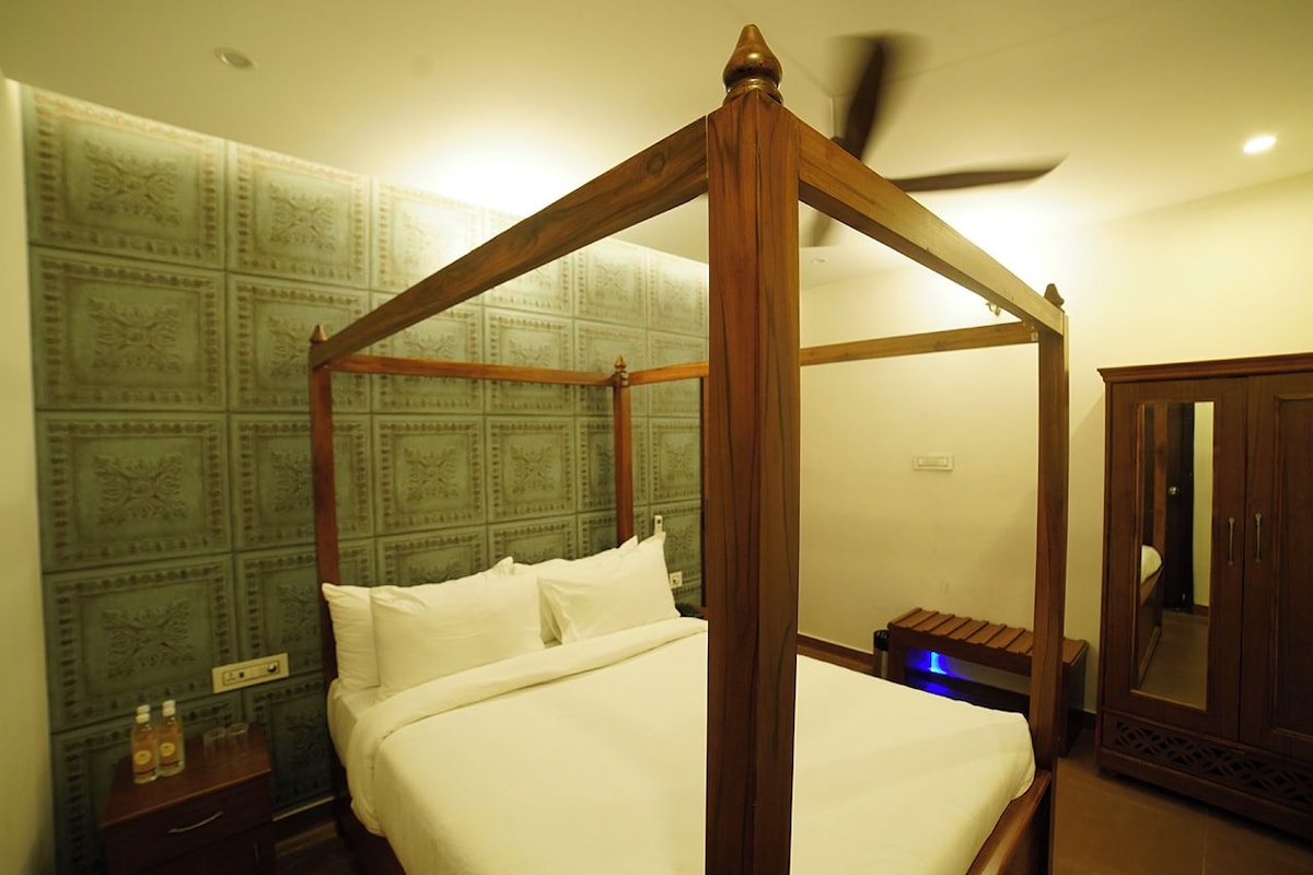 A four-poster bed with a wooden frame, a bedside table with a bottle and glasses, and a wardrobe with a mirror.