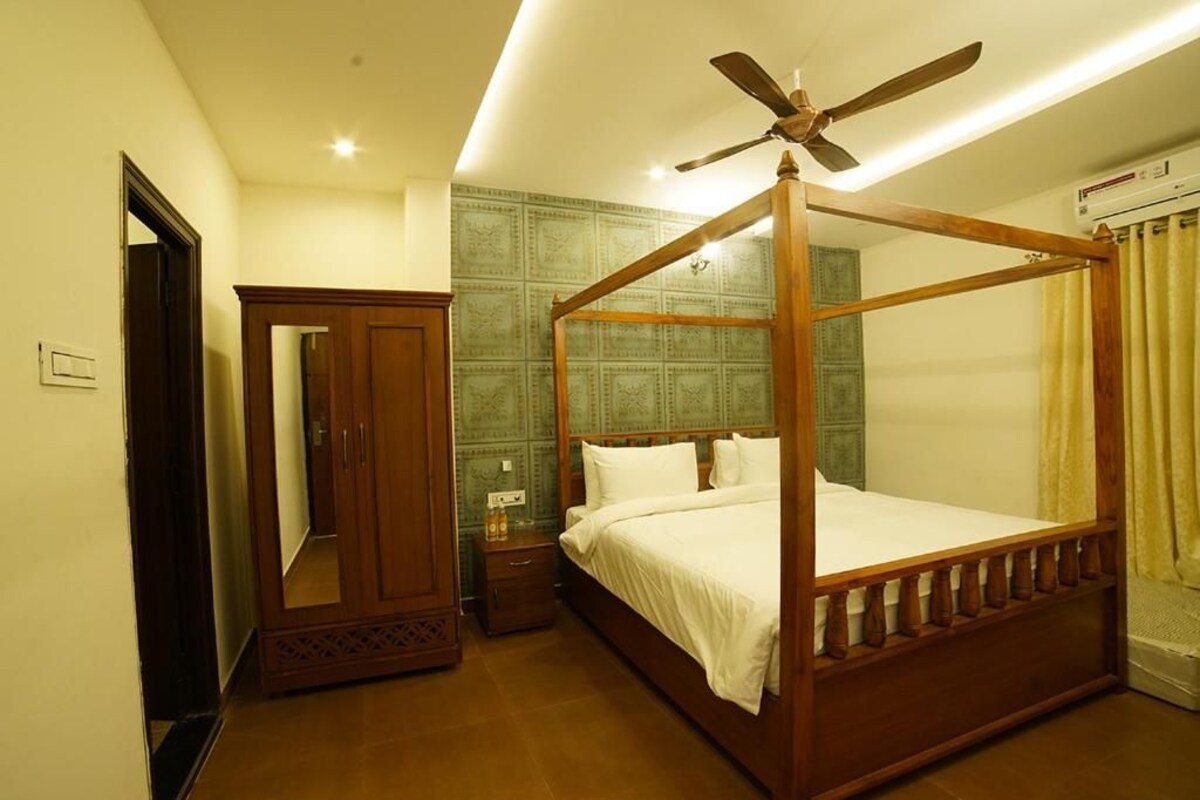 A four-poster bed with a ceiling fan, a wardrobe, and a mirror in a hotel room.