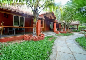 A red brick house with a tiled roof, a paved pathway, and a small garden area with grass and palm trees. - Brown Town Resort Spa and Convention (Hyderabad)