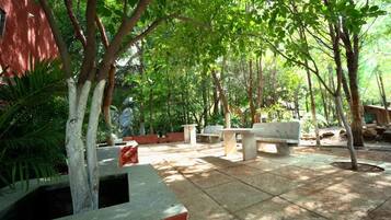 An outdoor patio area with stone flooring, benches, and trees providing shade.