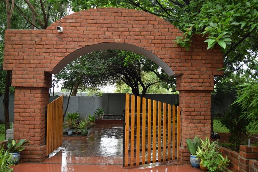 A brick archway with a wooden gate, surrounded by greenery and potted plants.