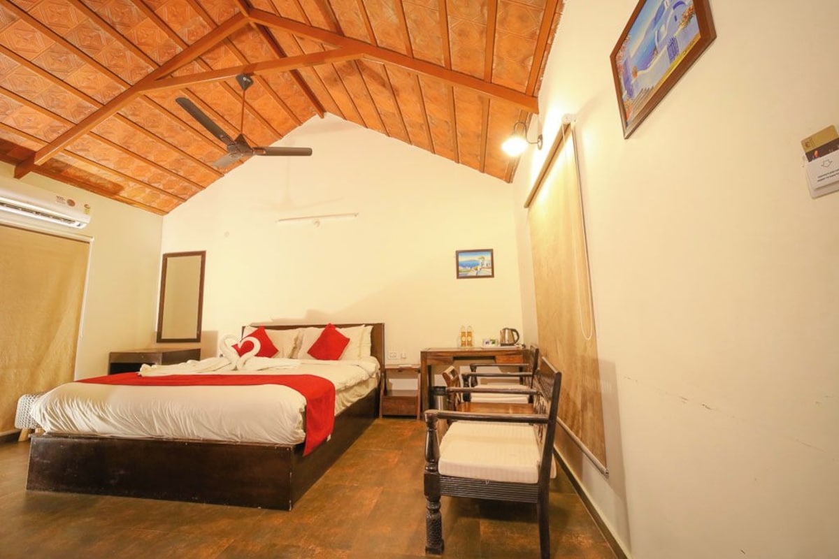 A bedroom with a wooden ceiling, a bed with red and white bedding, a nightstand, a chair, and a wall-mounted picture.