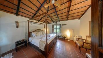 A four-poster bed with a wooden headboard, a bedside table, a chair, and a lamp.