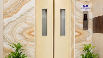 An elevator with a marble wall, a 4-person's max sign, and two potted plants.