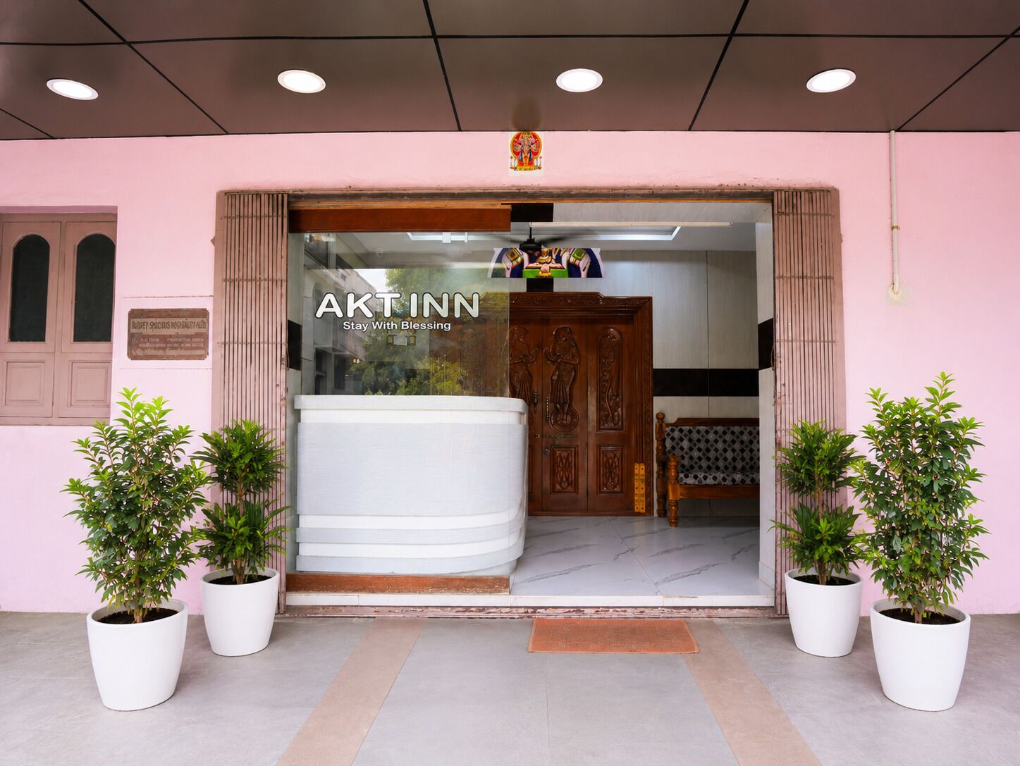 A hotel entrance with a sign reading 'AKTINN Stay With Blessing,' a wooden door, and potted plants.