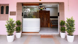 Entrada de hotel con un cartel que dice 'AKTINN Stay With Blessing', una puerta de madera y plantas en macetas.