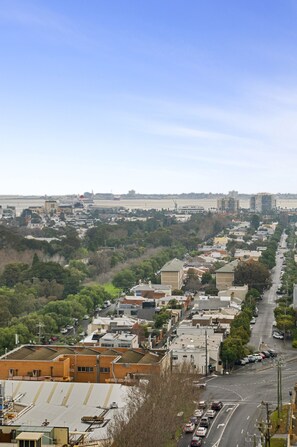 A cityscape with a mix of residential and commercial buildings, a clear sky, and a distant body of water. - Elevated 1-Bed Apartment Near Melbourne CBD (South Melbourne)
