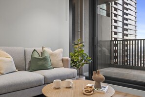 Ein modernes Wohnzimmer mit grauem Sofa, einem Couchtisch und Blick auf ein Hochhaus.