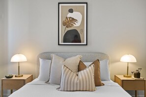 A bedroom with a bed, two bedside tables, two lamps, and a framed artwork on the wall. - Elevated 1-Bed Apartment Near Melbourne CBD (South Melbourne)