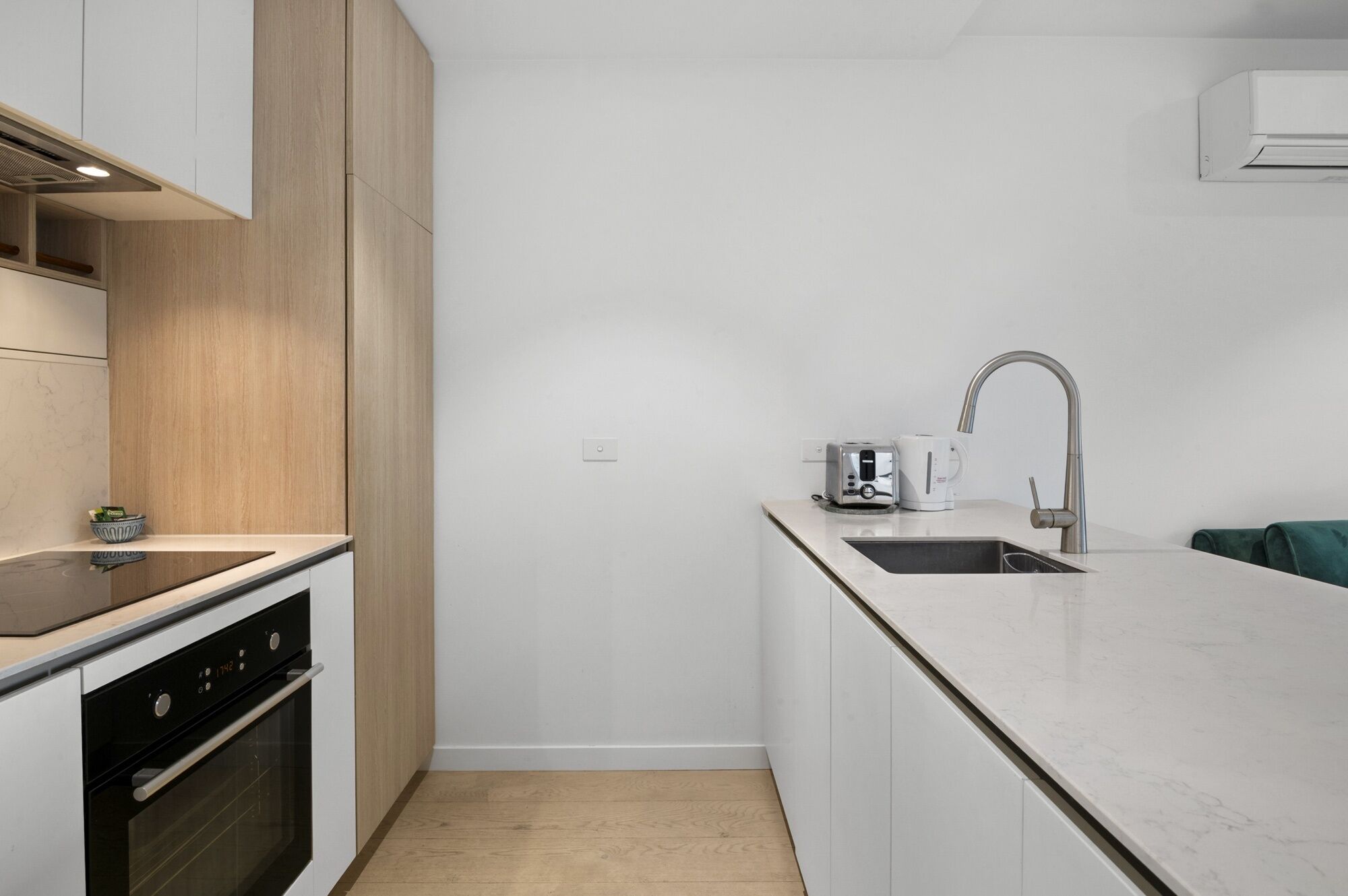 A compact kitchen with a built-in oven, a sink with a modern faucet, and a coffee maker on the countertop.