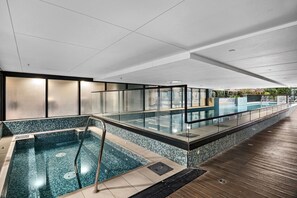 Ein moderner, überdachter Pool mit Glasgeländern und einer Holzterrasse.