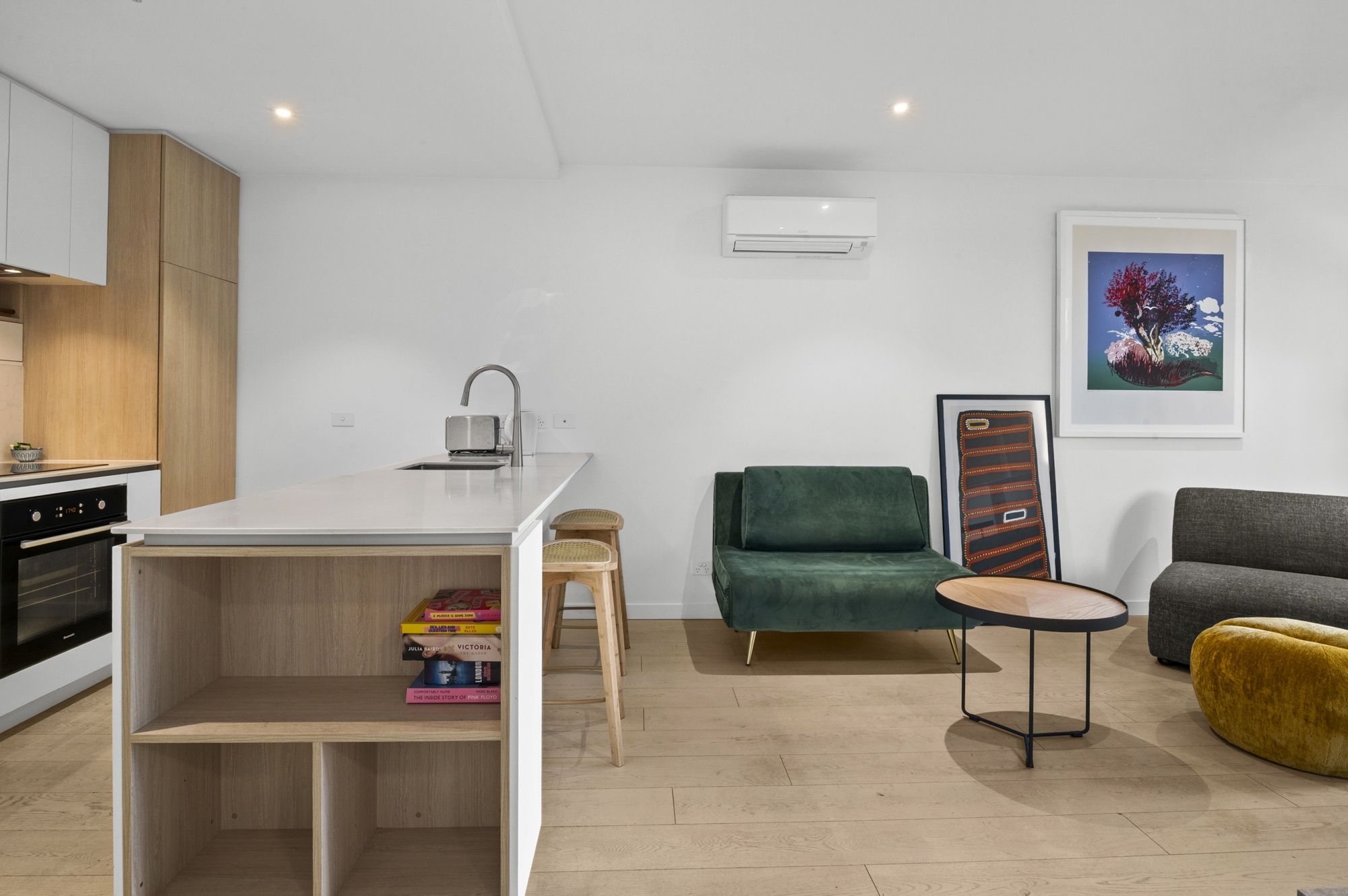 A modern kitchen with a built-in oven, a small island with a sink, and a wooden shelf with books.
