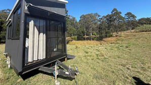 A small, modern, black cabin with a sliding glass door, situated in a grassy field with trees in the background. - Hamilton Country Retreat 1 by Tiny Away (Kangaroo Valley)