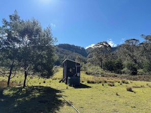 A small cabin in a grassy field with trees and mountains in the background.