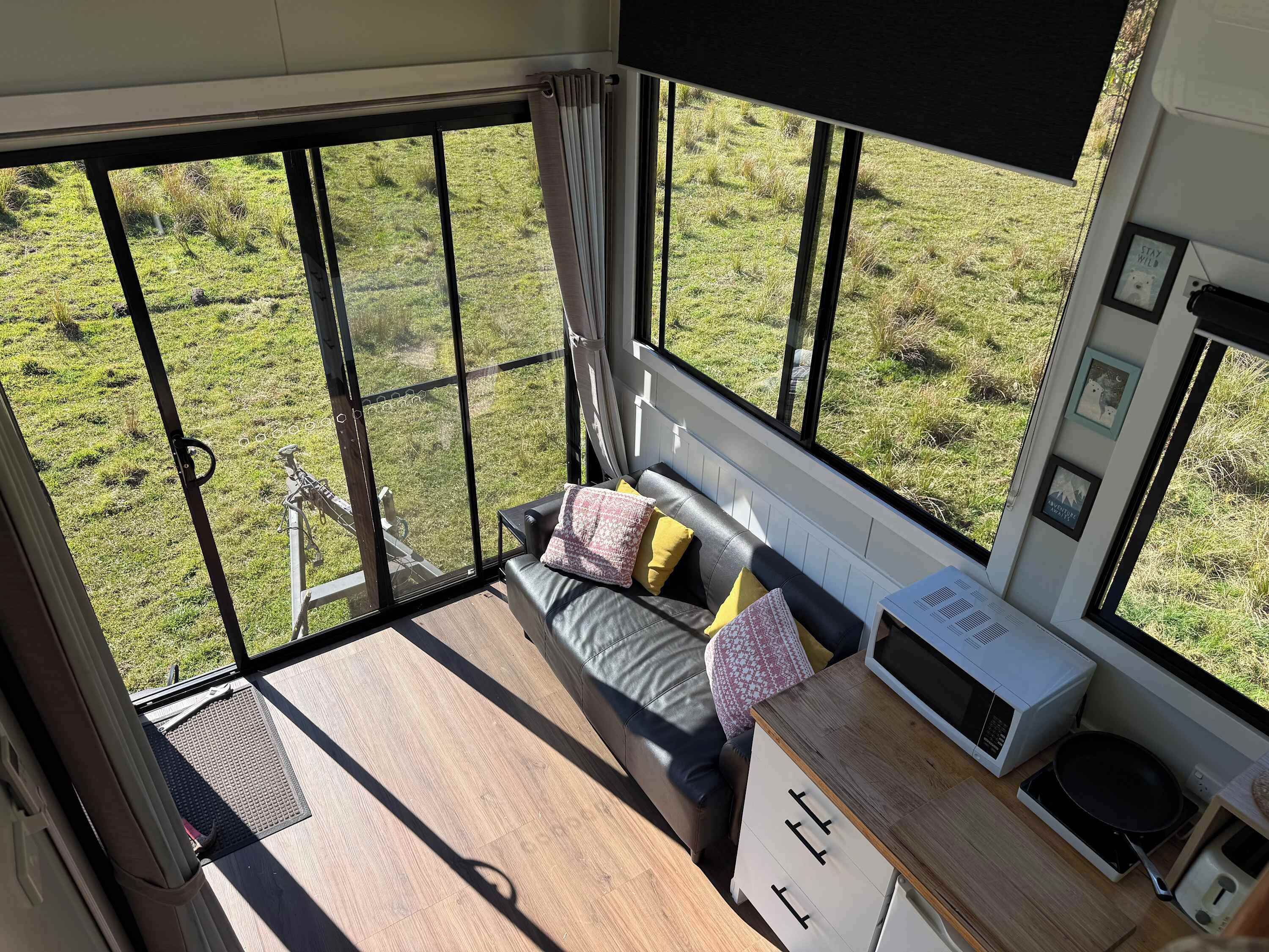 Een kamer met een bed, een klein tafeltje, een magnetron en uitzicht op een grasveld door grote ramen.
