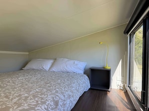 Un dormitorio con una cama, una mesita de noche, una lámpara y una ventana.