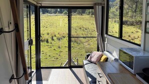 A room with a large sliding glass door leading to a grassy field, a sofa with cushions, and a microwave on the counter. - Hamilton Country Retreat 1 by Tiny Away (Kangaroo Valley)