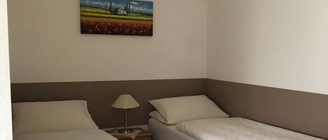 A hotel room with two beds, a nightstand, a lamp, and a painting on the wall.