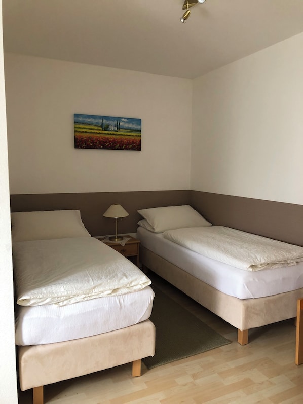 A hotel room with two beds, a nightstand, a lamp, and a painting on the wall.