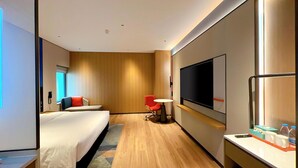 Una habitación de hotel moderna con cama, escritorio, silla, televisor y minibar.