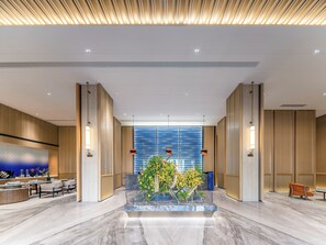 Un vestíbulo moderno con un mostrador de recepción de mármol, zona de estar y un arreglo floral central.