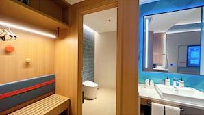 Un baño moderno con un banco de madera, inodoro y zona de lavamanos con artículos de aseo.