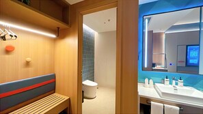 Un baño moderno con un banco de madera, inodoro y zona de lavamanos con artículos de aseo.
