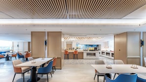 Un comedor moderno con mesas y sillas, una cocina al fondo y vistas de la ciudad.