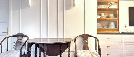 A room with a round wooden table, two upholstered chairs, a white door with a brass handle, and a wooden cabinet with glass doors.
