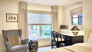 A hotel room with a bed, a desk with a lamp, a chair, a small table with a book, and a window with curtains. - Mapleton Hill Guest Suite in Boulder Historic District - few steps from Pearl St (Boulder)