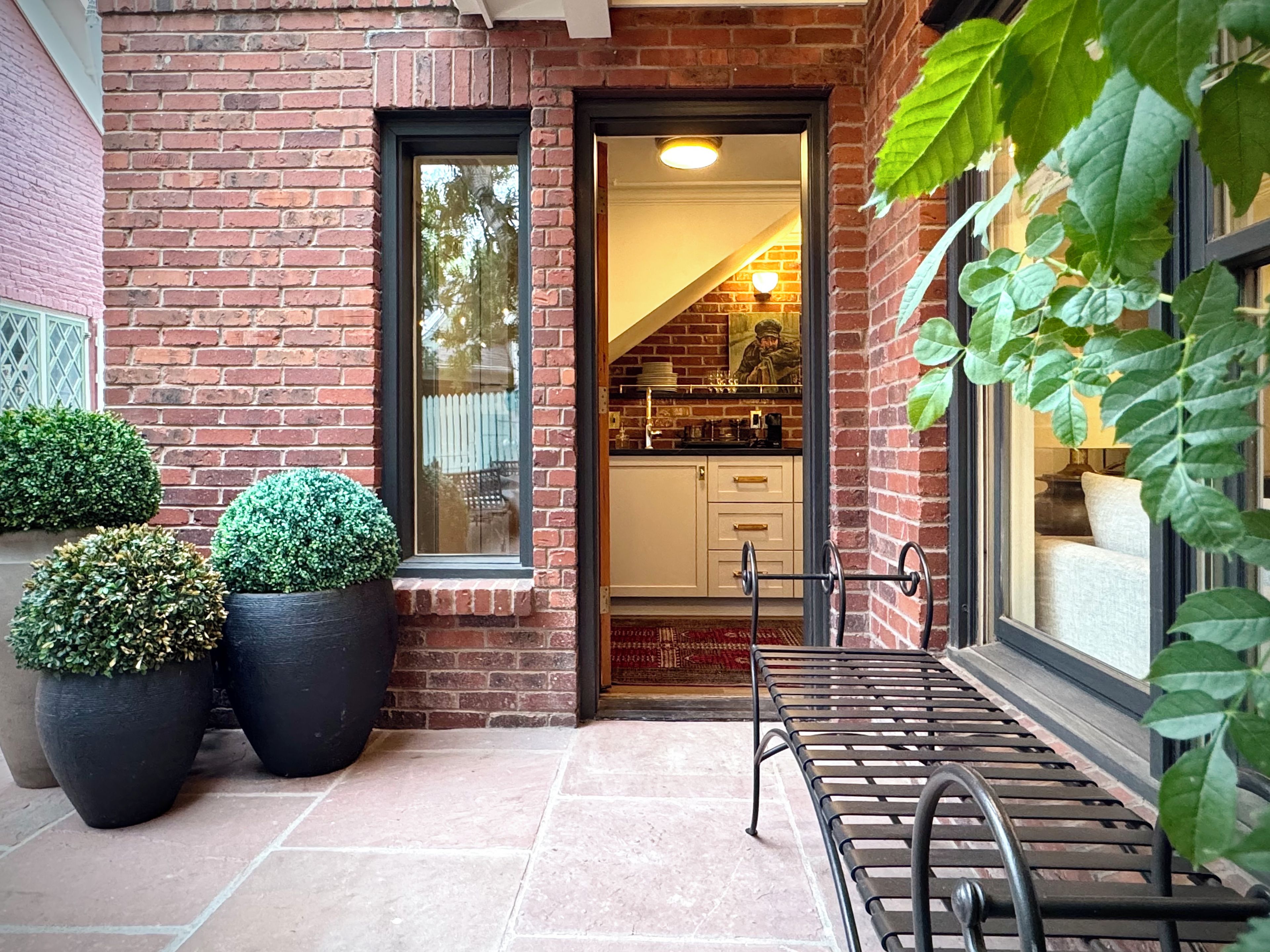 A brick building with a glass door entrance, potted plants, and a metal bench outside.