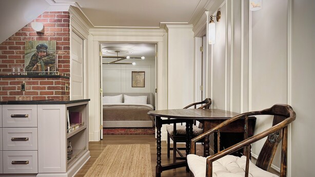 A room with a bed, a dining table with chairs, a kitchen area with a brick wall and a painting, and a hallway leading to another room. - Mapleton Hill Guest Suite in Boulder Historic District - few steps from Pearl St (Boulder)