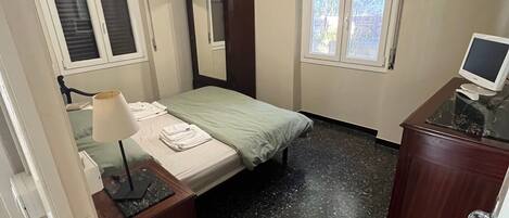 A bedroom with a bed, a desk with a computer, a mirror, and two windows.