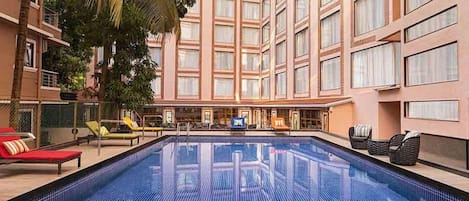 An indoor swimming pool with lounge chairs and a view of a high-rise building.